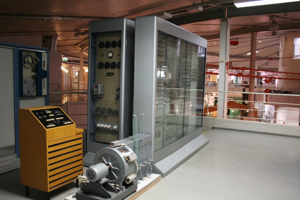 Suuri tietokone. Korkeat harmaat laatikot ja ohjauspaneli.