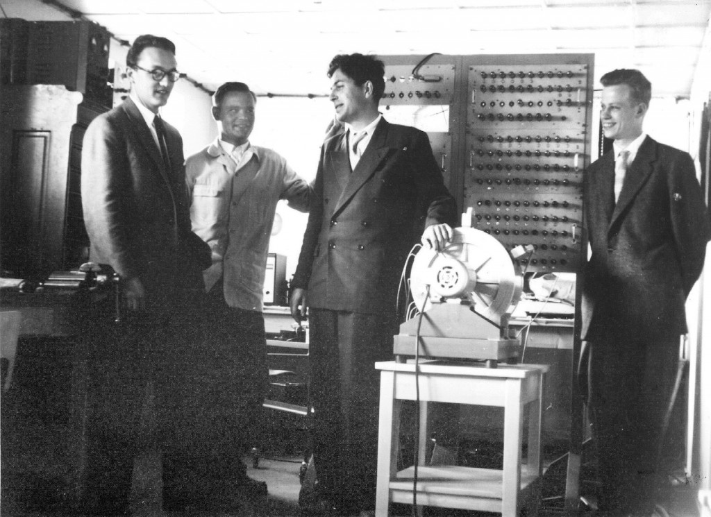 Neljä miestä seisoo tietokoneen edessä.