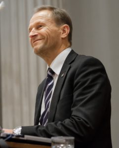 Hymyilevä mieshenkilö puhujapöntön takana.