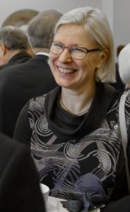 Hymyilevä nainen kahvipöydässä.
